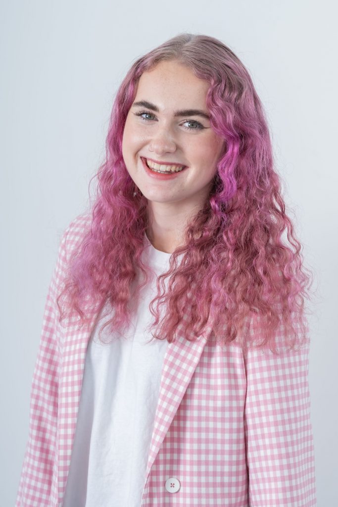 Portrait image of Hannah smiling wearing a pink and white checkered blazer