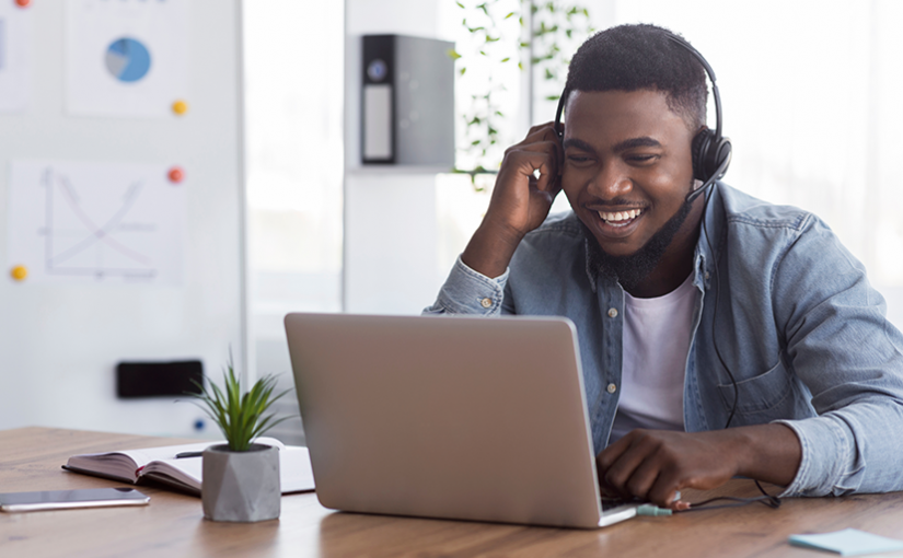 male laughing at his laptop wearing headphones